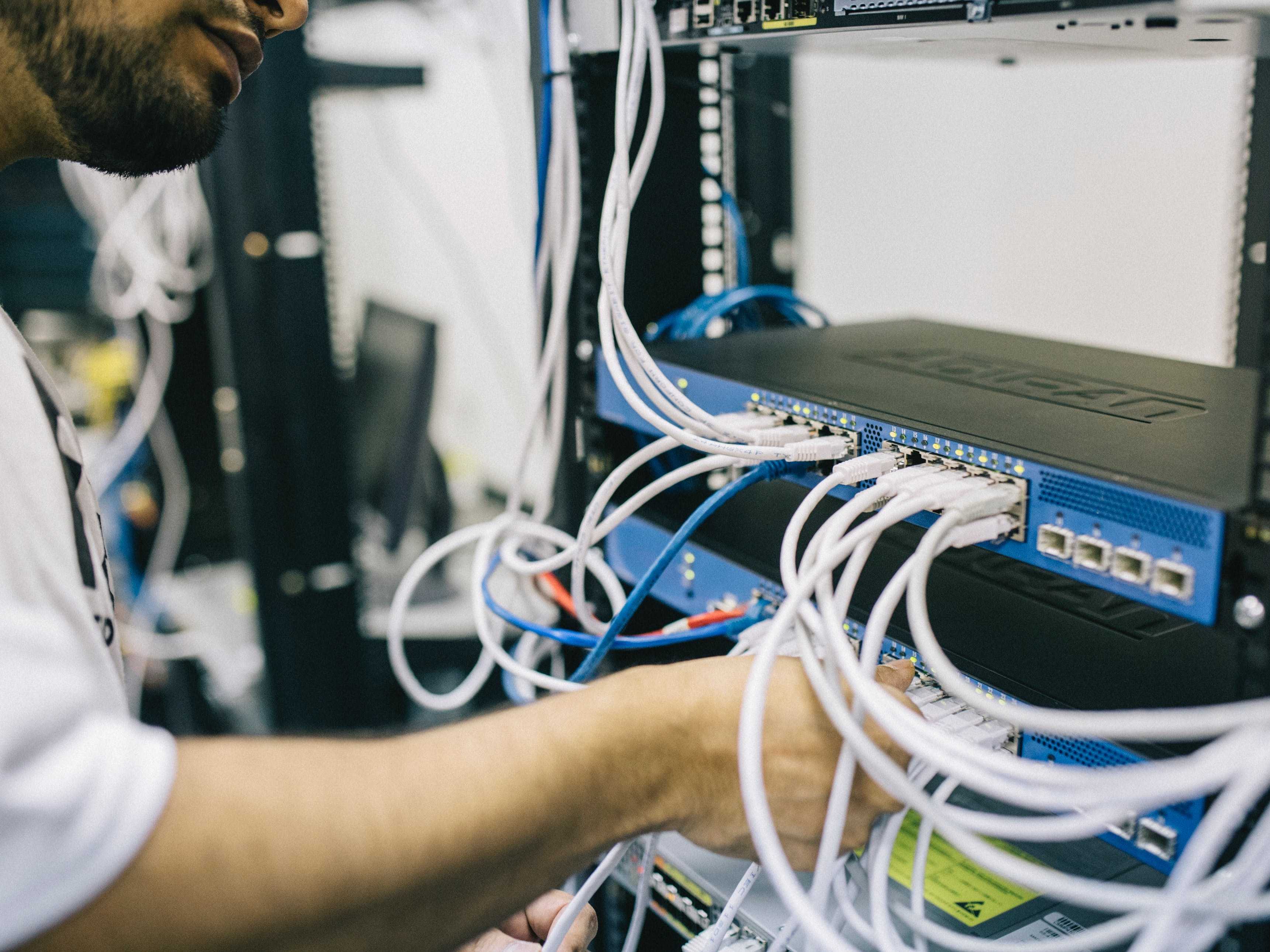Man working on a network switch by plugging in ethernet cable