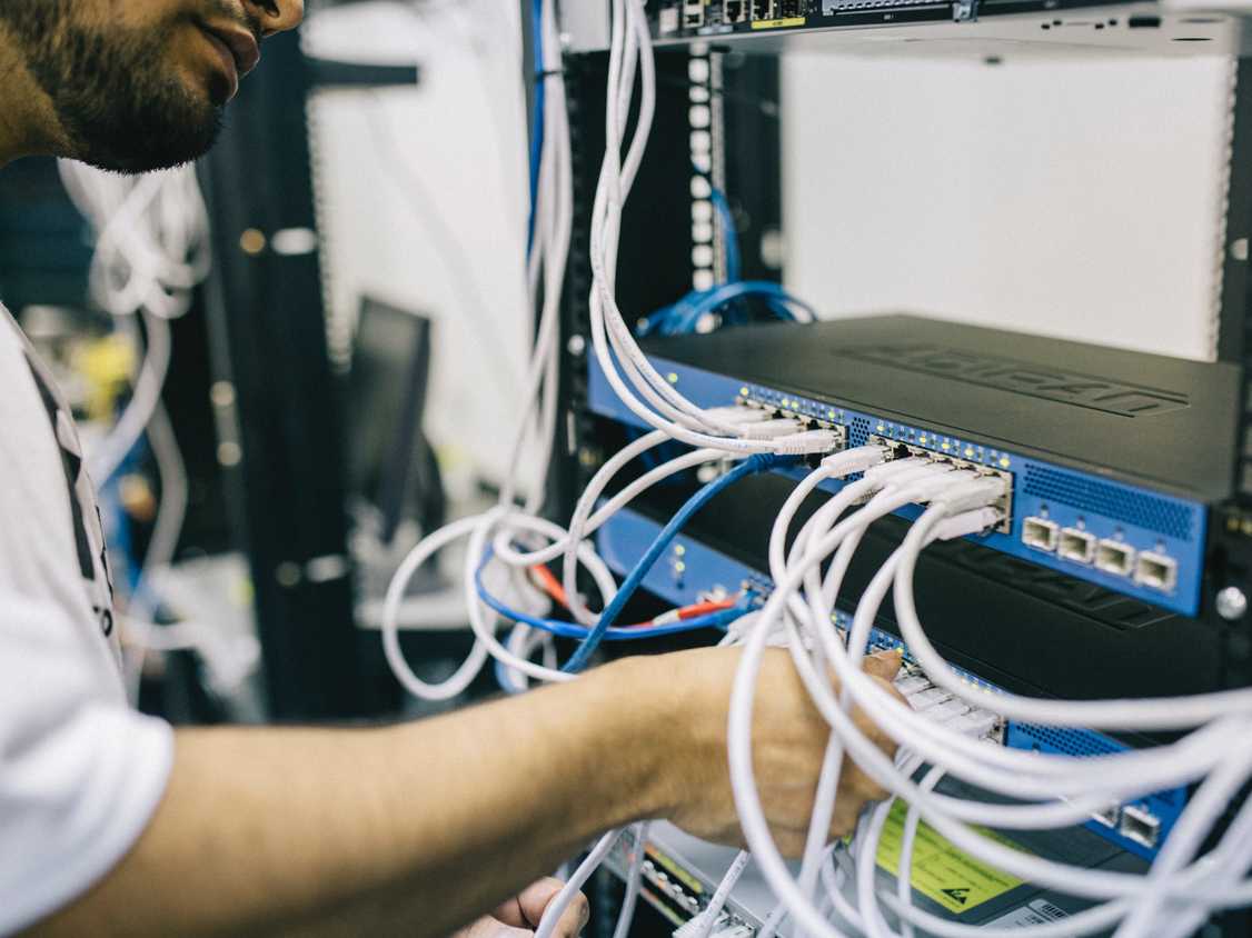 Man working on a network switch by plugging in ethernet cable
