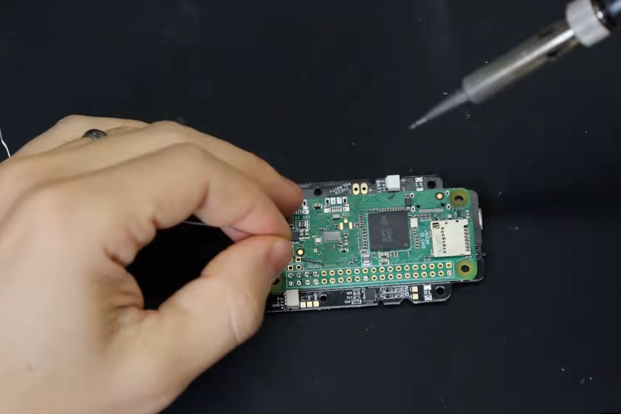 A screenshot showing a person soldering a Raspberry Pi module to onto a PCB.