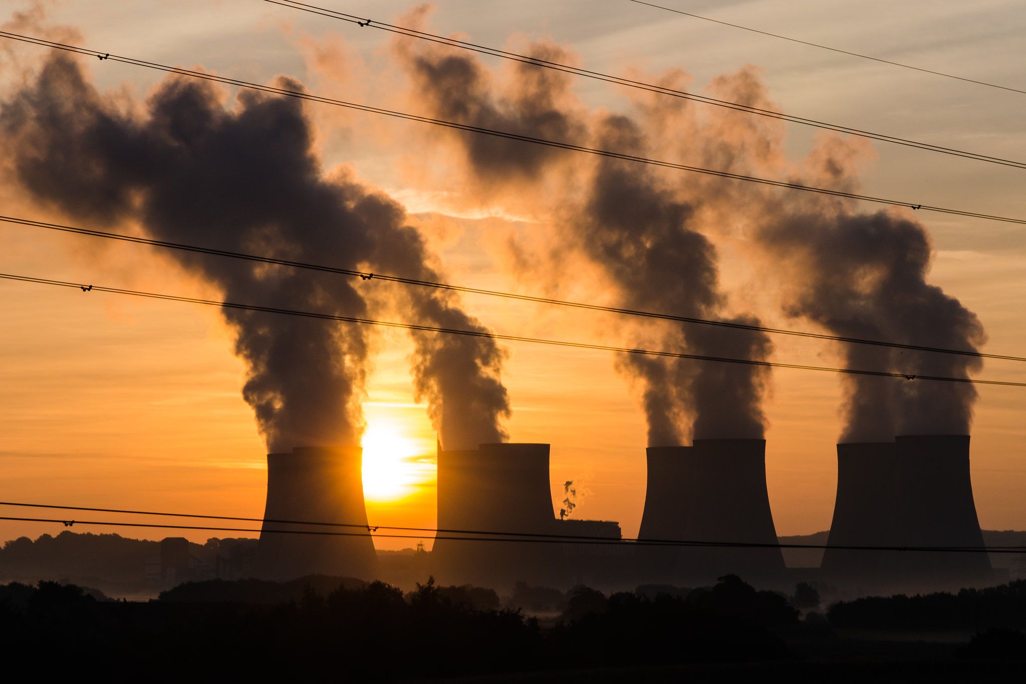 Power plant emitting smoke in the distance with the Sun in the background