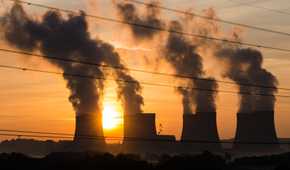 Power plant emitting smoke in the distance with the Sun in the background