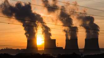 Power plant emitting smoke in the distance with the Sun in the background