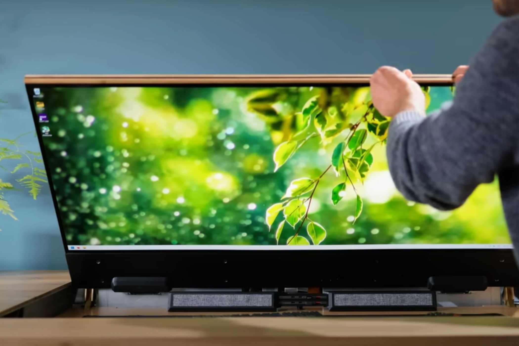 A person lifting a piece of wodden slab revealing a monitor and peripheral hiding underneat it