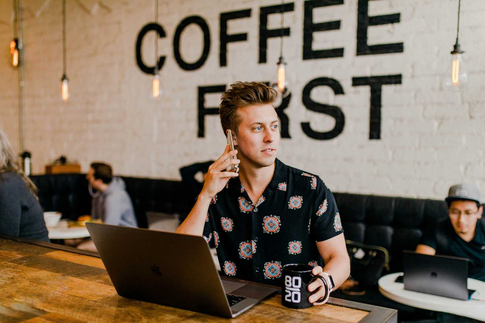 Person in coffee shop with laptop and on phone