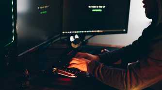 Crop hacker silhouette typing on computer keyboard while hacking system