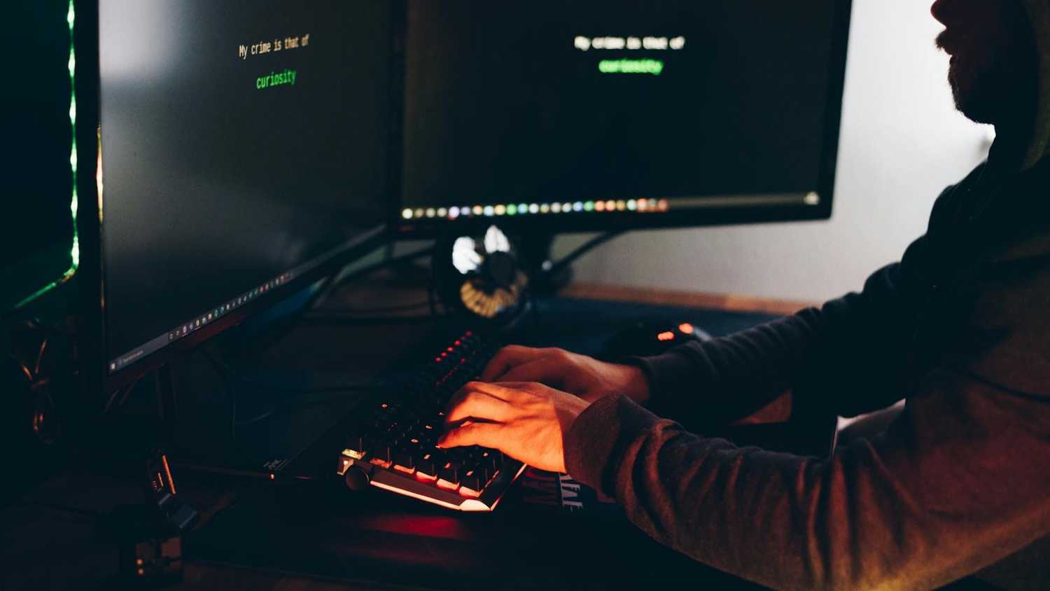 Hacker typing on a keyboard sitting in the dark