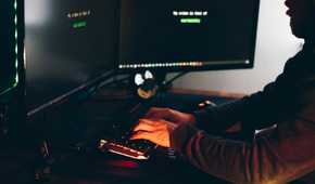 Hacker typing on a keyboard sitting in the dark