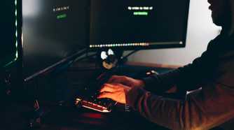 Hacker typing on a keyboard sitting in the dark