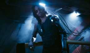 A screenshot from Cyberpunk 2077: Phantom Liberty, showing Johnny Silverhand, played by Keanu Reeves, leaning against a railing as he looks at the protagonist.