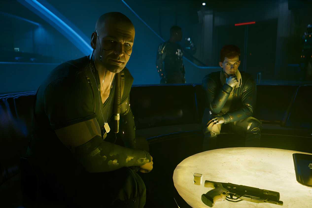 A screenshot from Cyberpunk 2077: Phantom Liberty, showing Kurt Hansen, the DLC's antagonist, sitting with the protagonist and another character at a warmly-lit table.