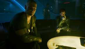 A screenshot from Cyberpunk 2077: Phantom Liberty, showing Kurt Hansen, the DLC's antagonist, sitting with the protagonist and another character at a warmly-lit table.