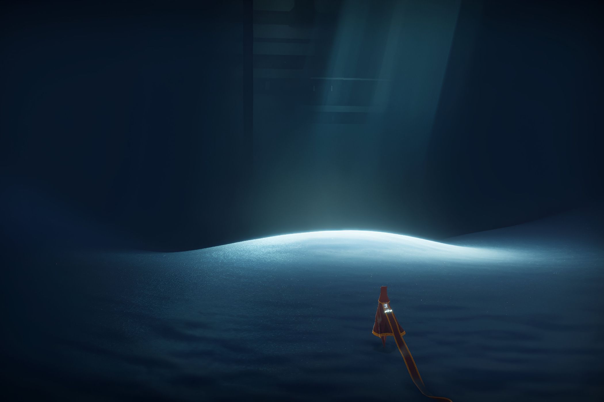 A screenshot from the game Journey, showing the protagonist walk across sand in a dark room, with sunlight peering through.