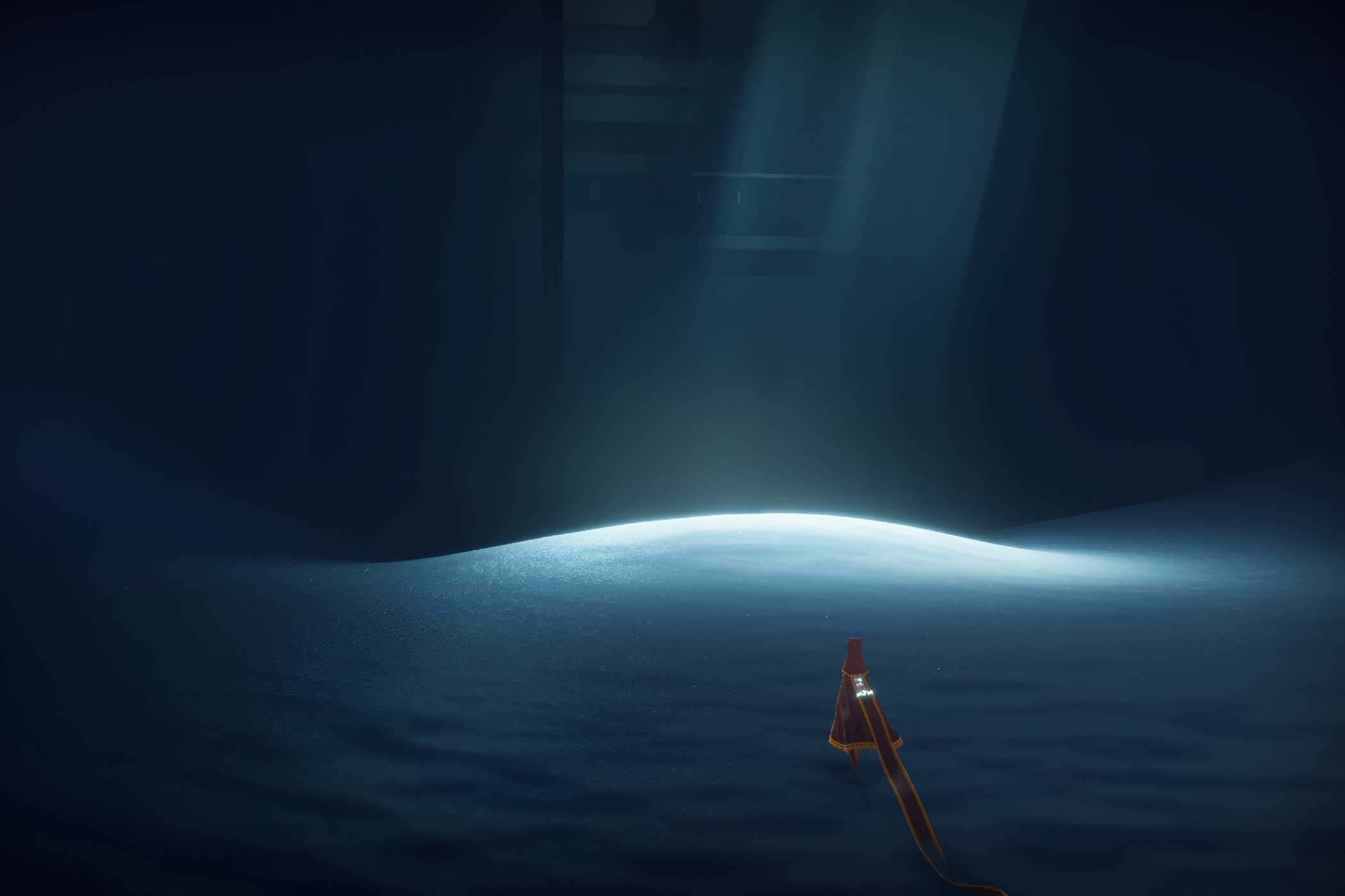 A screenshot from the game Journey, showing the protagonist walk across sand in a dark room, with sunlight peering through.
