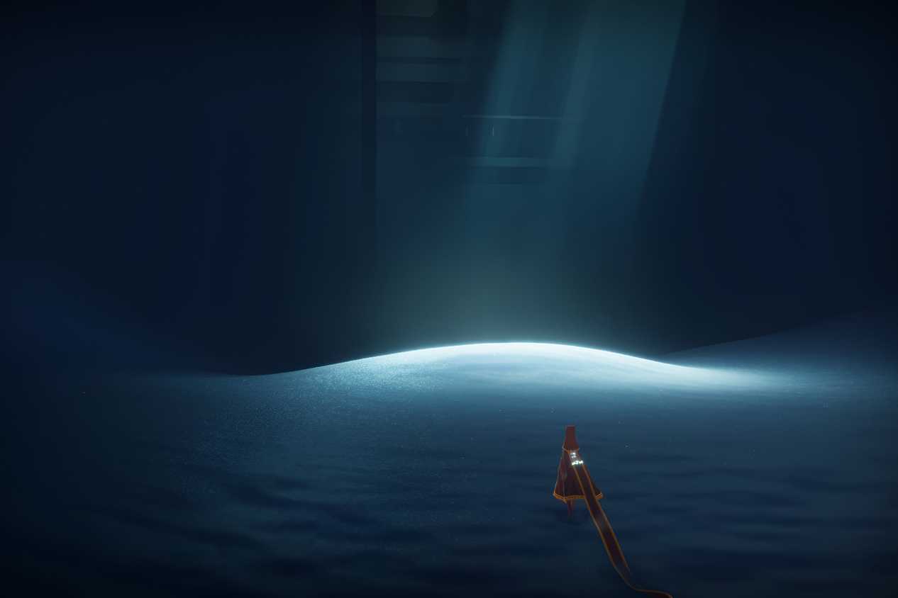 A screenshot from the game Journey, showing the protagonist walk across sand in a dark room, with sunlight peering through.