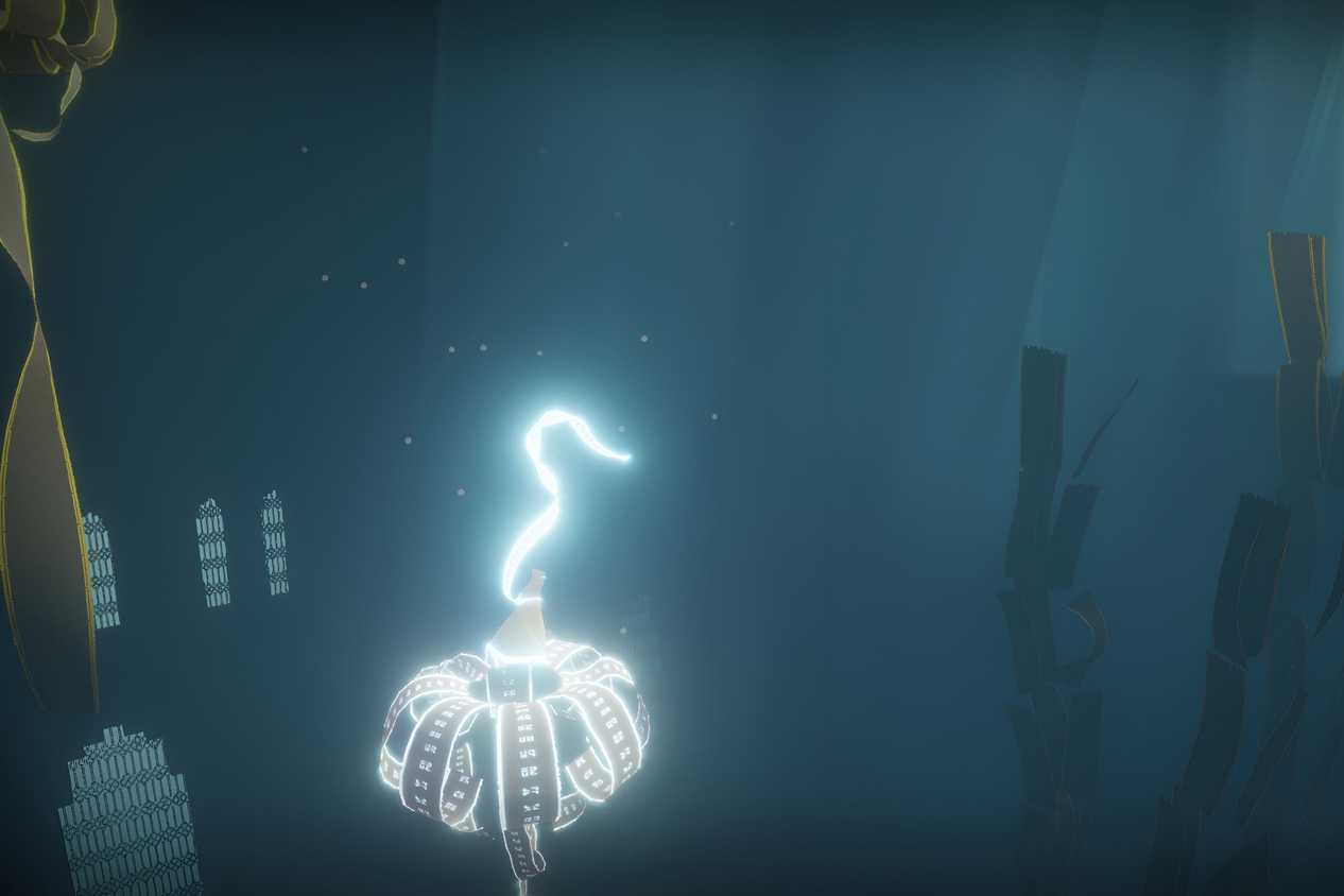 A screenshot from the game Journey, showing the protagonist's robes glow as they float through a dark, blue, environment.