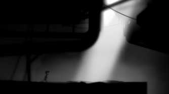 A screenshot from the game Limbo showing sunlight breaking into the dark, eerie, black-and-white environment as the protagonist runs towards it.