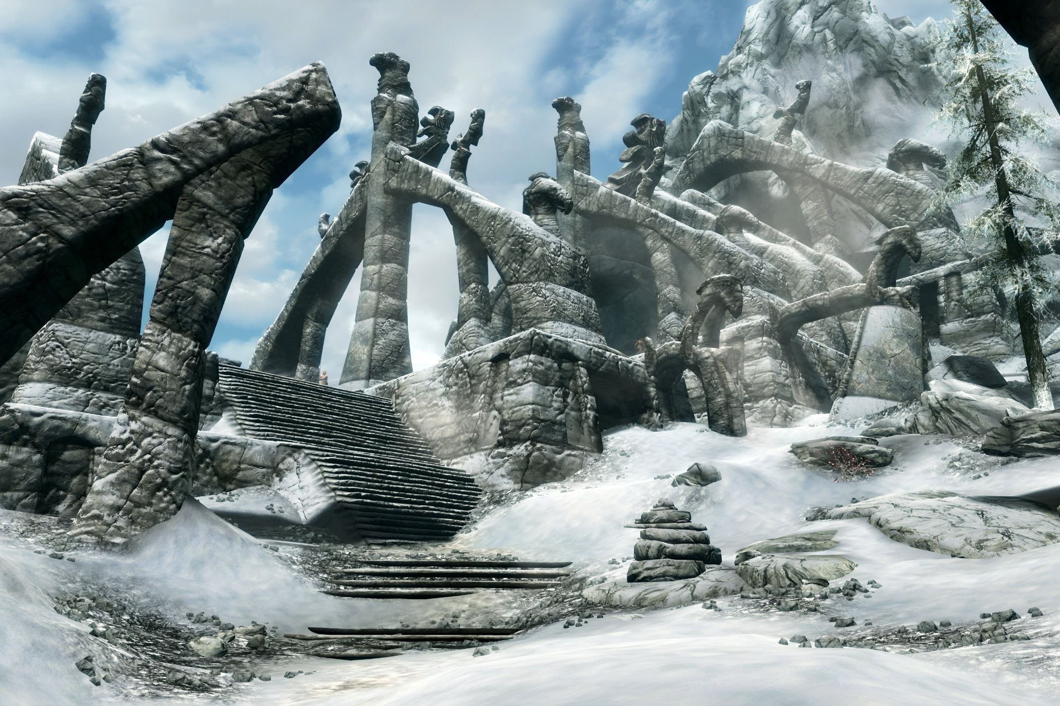 A screenshot from the game The Elder Scrolls V: Skyrim, showing ruins of a huge structure, covered in parts in snow.