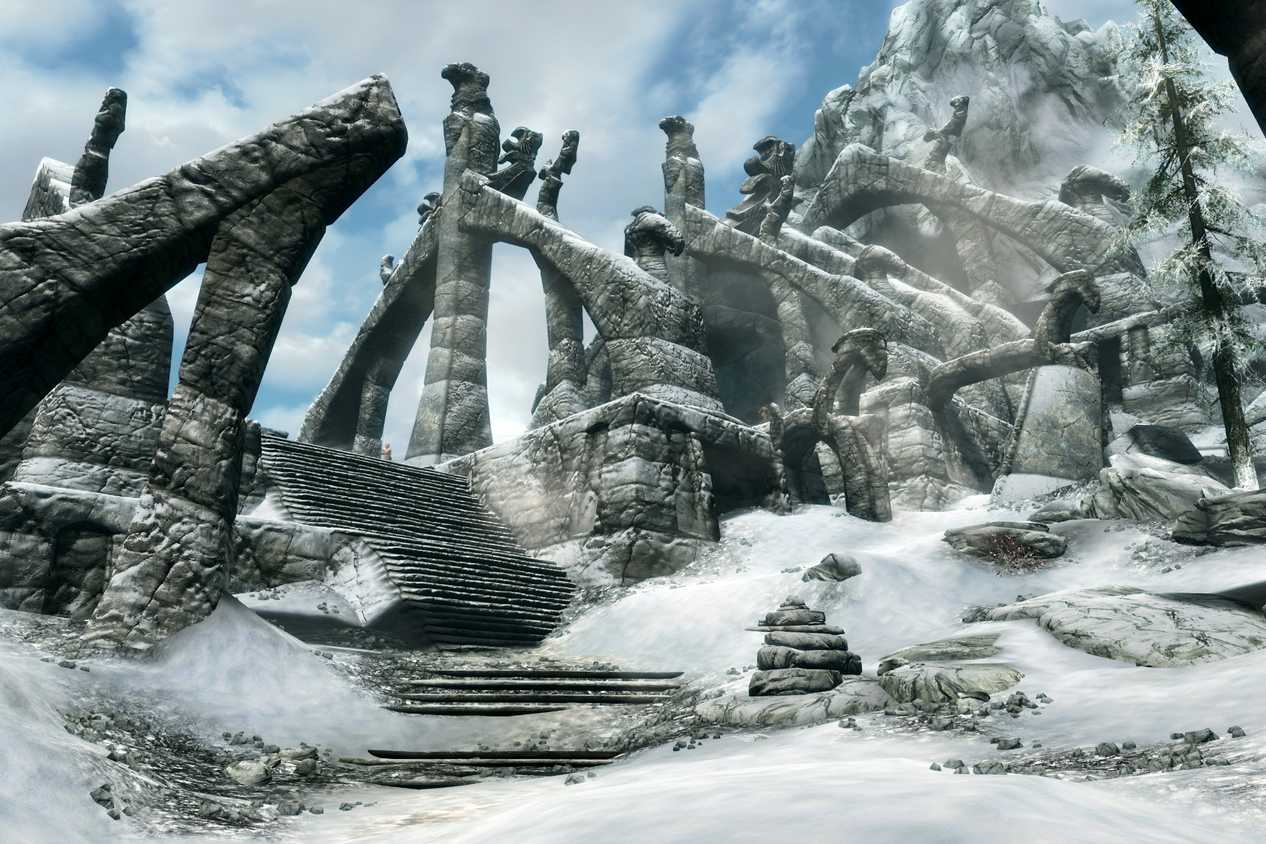 A screenshot from the game The Elder Scrolls V: Skyrim, showing ruins of a huge structure, covered in parts in snow.