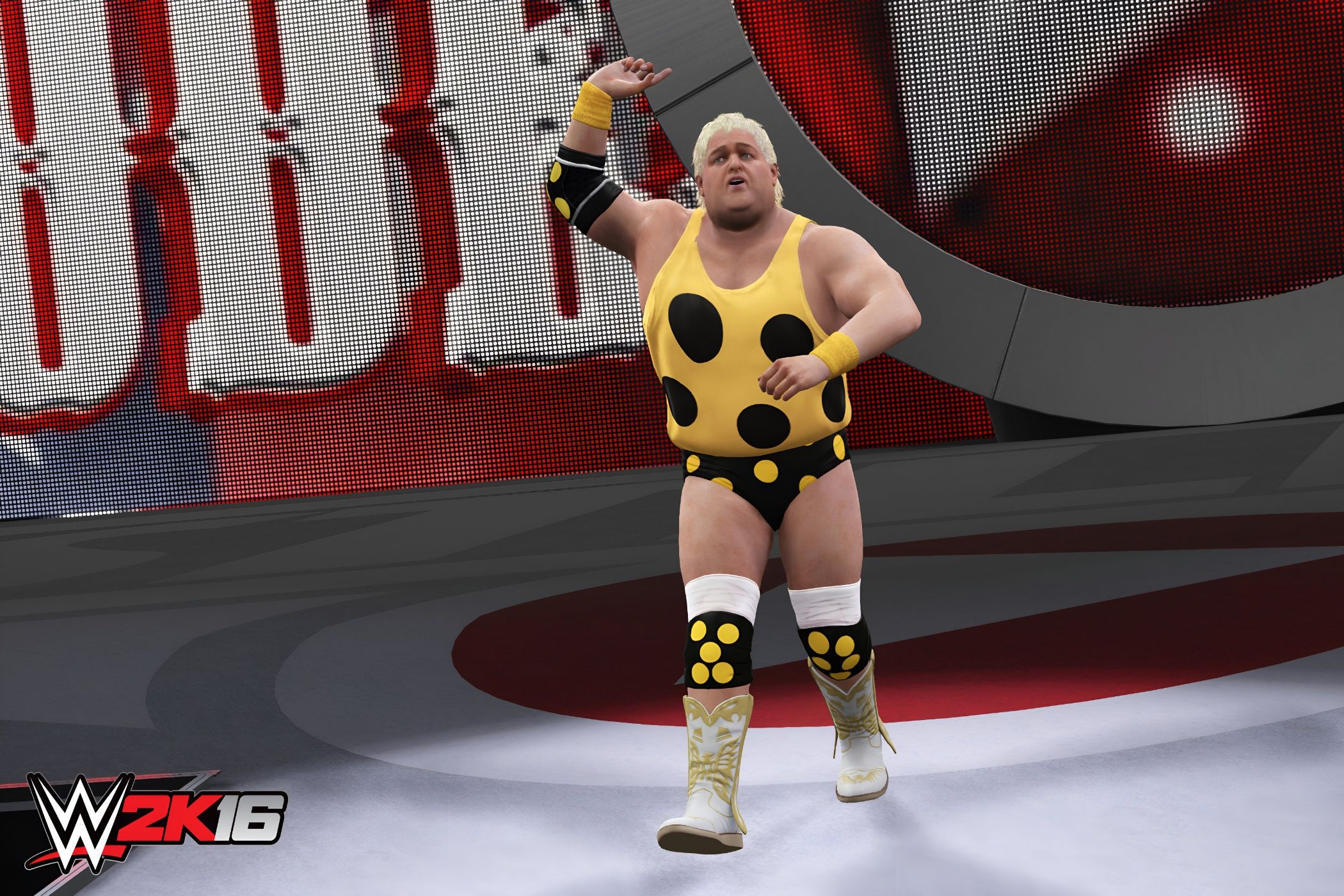 A screenshot from WWE 2K16, showing Dusty Rhodes, a healthy old man with short blonde hair, wearing a polka-dotted yellow outfit, enter the arena while raising one hand in the air.