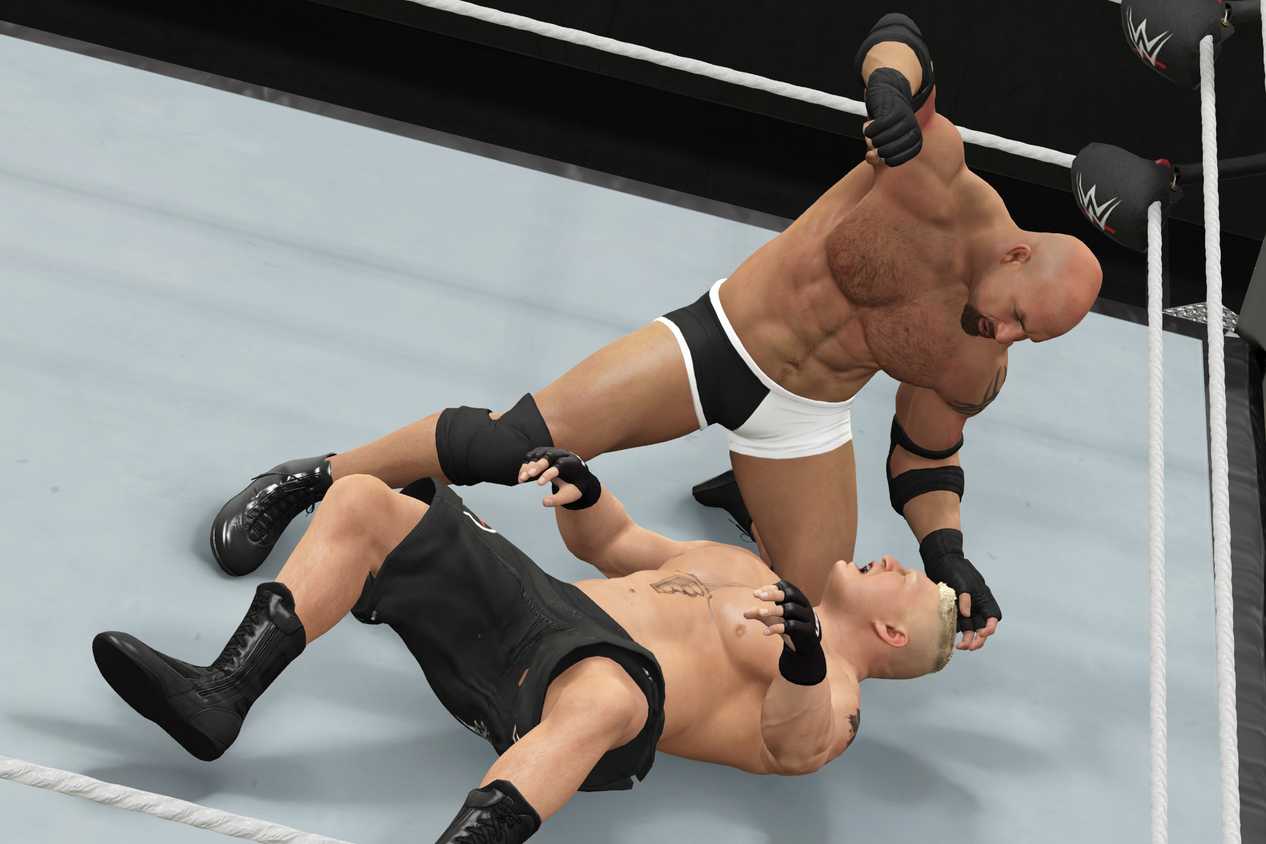 A screenshot from WWE 2K17, showing WWE superstar Goldberg attack Brock Lesnar (black shorts) while he's on the ground.
