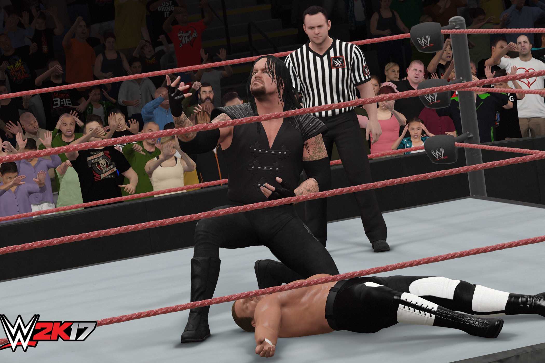 A screenshot from WWE 2K17, showing the Undertaker, in black overalls, lean over a knocked out Hunter Hearst Helmsley.