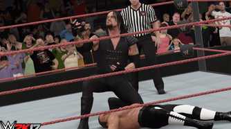 A screenshot from WWE 2K17, showing the Undertaker, in black overalls, lean over a knocked out Hunter Hearst Helmsley.
