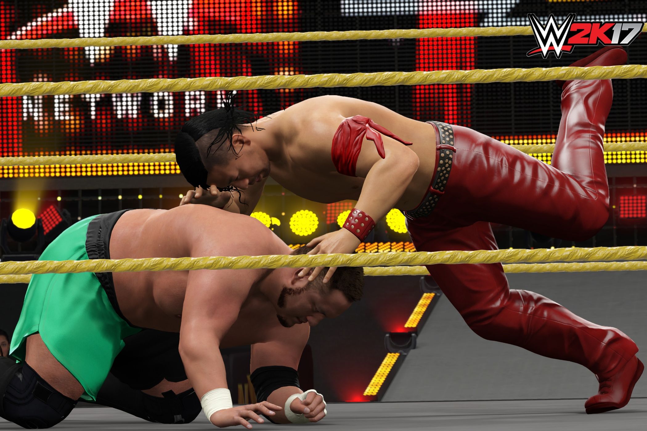 A screenshot from WWE 2K17, showing Shinsuke Nakamura attack a crouched Samoa Joe wearing green shorts.
