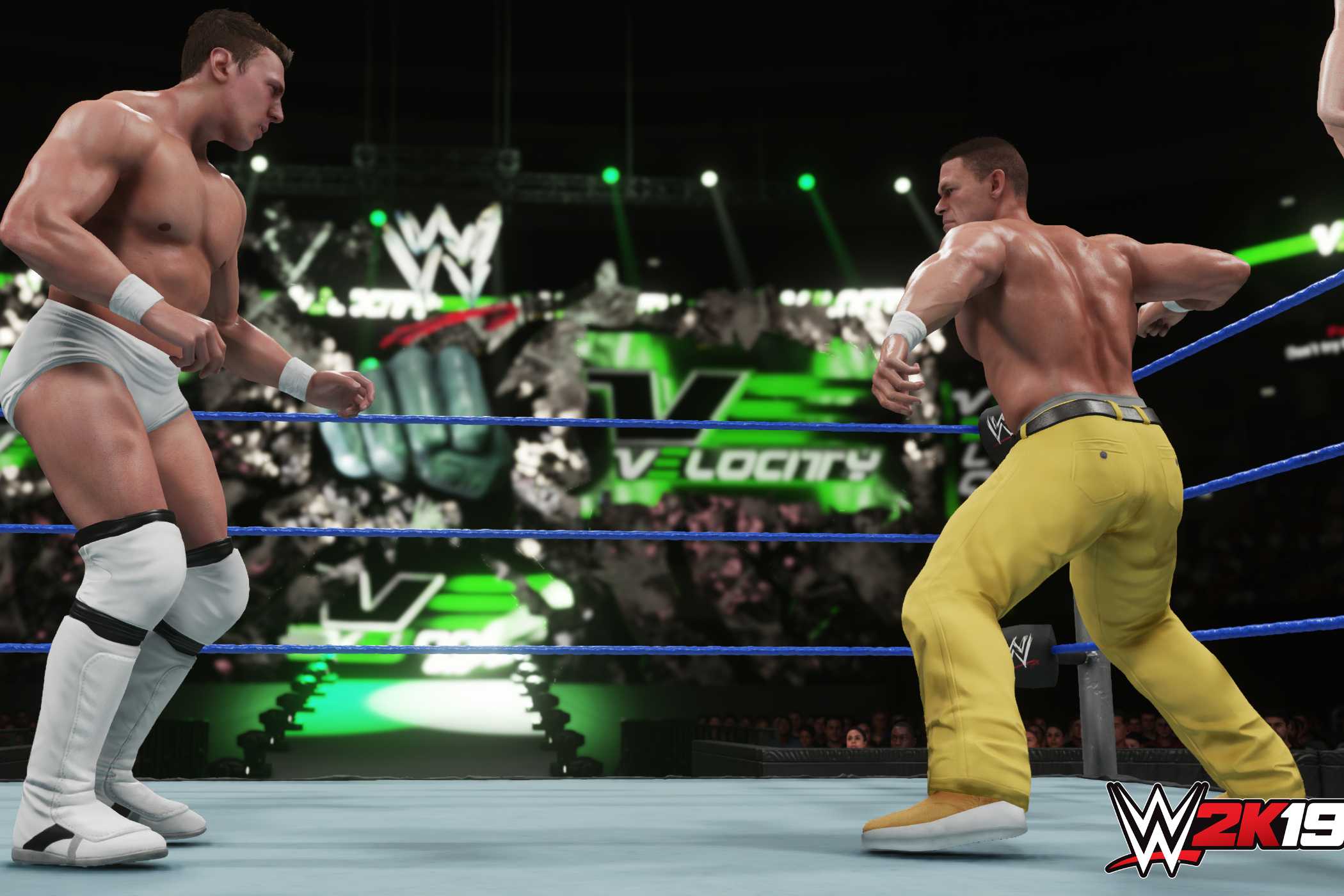 A screenshot from WWE 2K19, showing John Cena, wearing yellow pants, face off against Bryan Danielson in white tights, inside the ring.