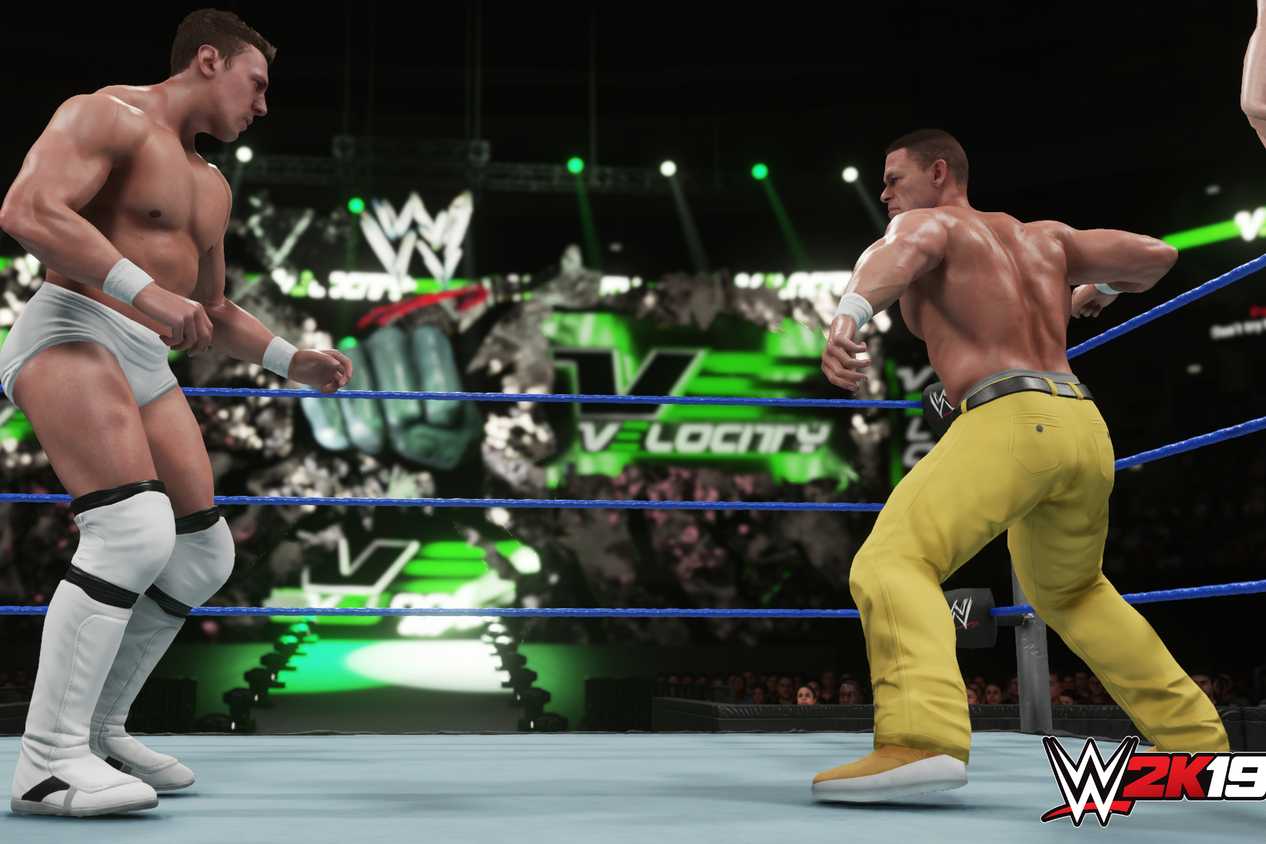 A screenshot from WWE 2K19, showing John Cena, wearing yellow pants, face off against Bryan Danielson in white tights, inside the ring.