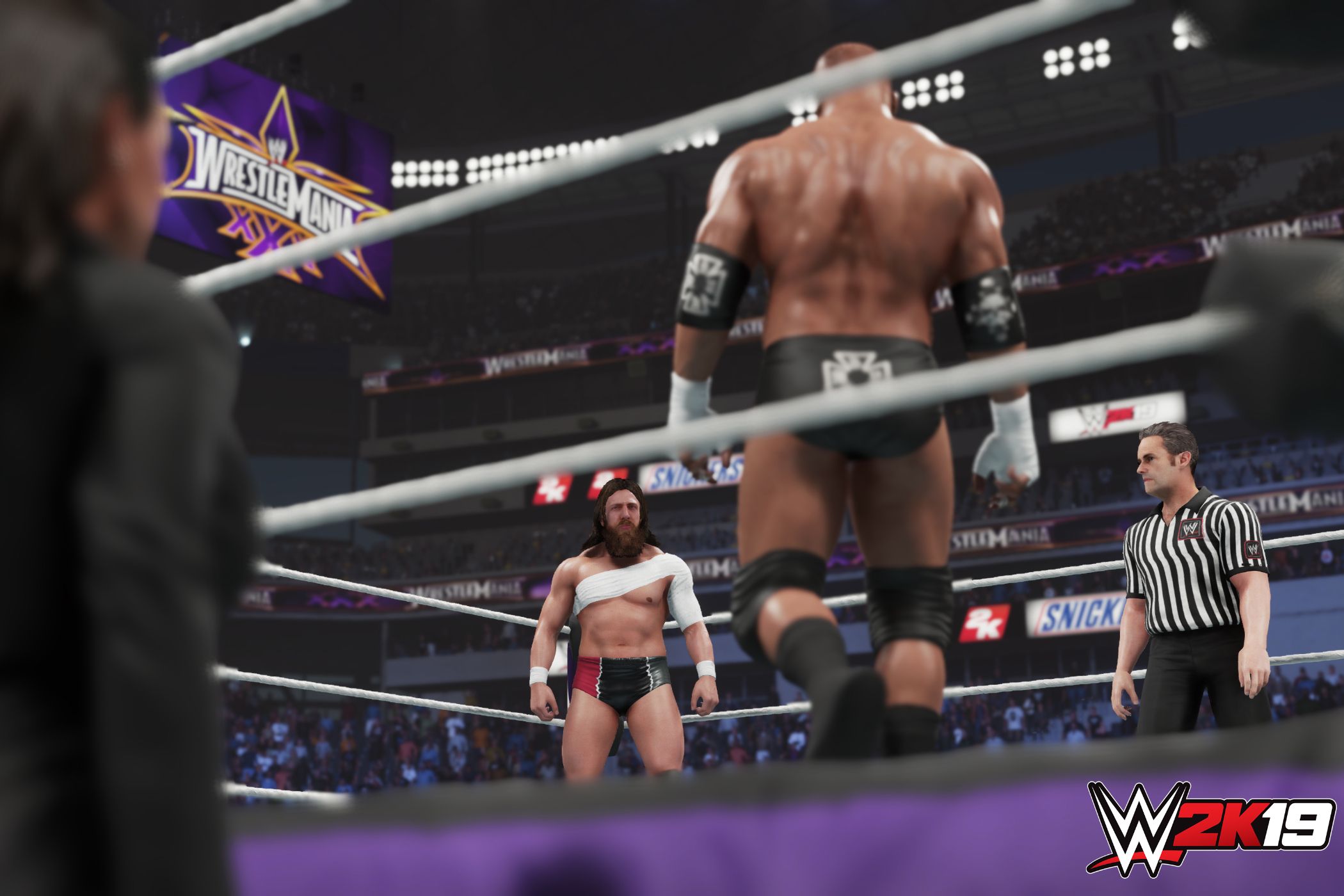 A screenshot from WWE 2K19, showing a bald Triple H face off against a bandaged Daniel Bryan in the ring as a referee looks on inside the ring.