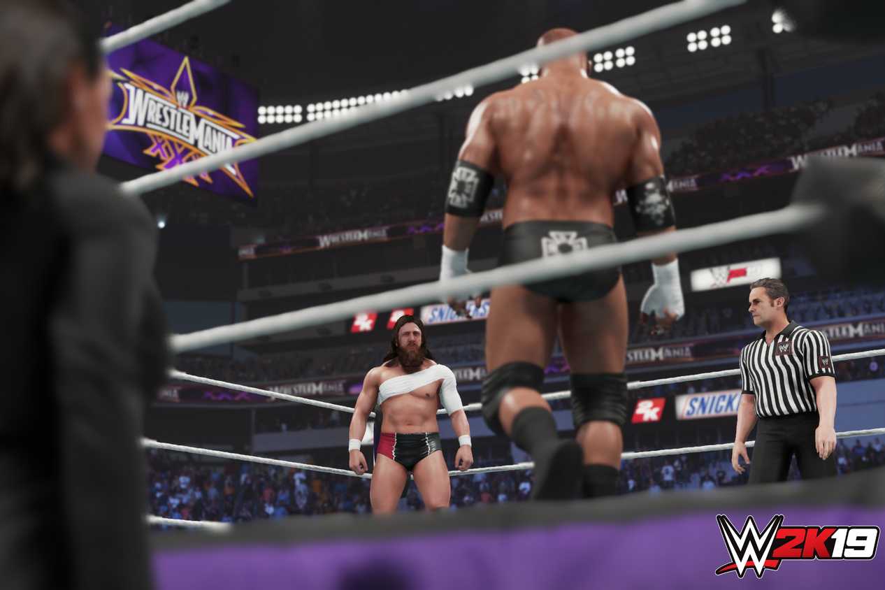 A screenshot from WWE 2K19, showing a bald Triple H face off against a bandaged Daniel Bryan in the ring as a referee looks on inside the ring.