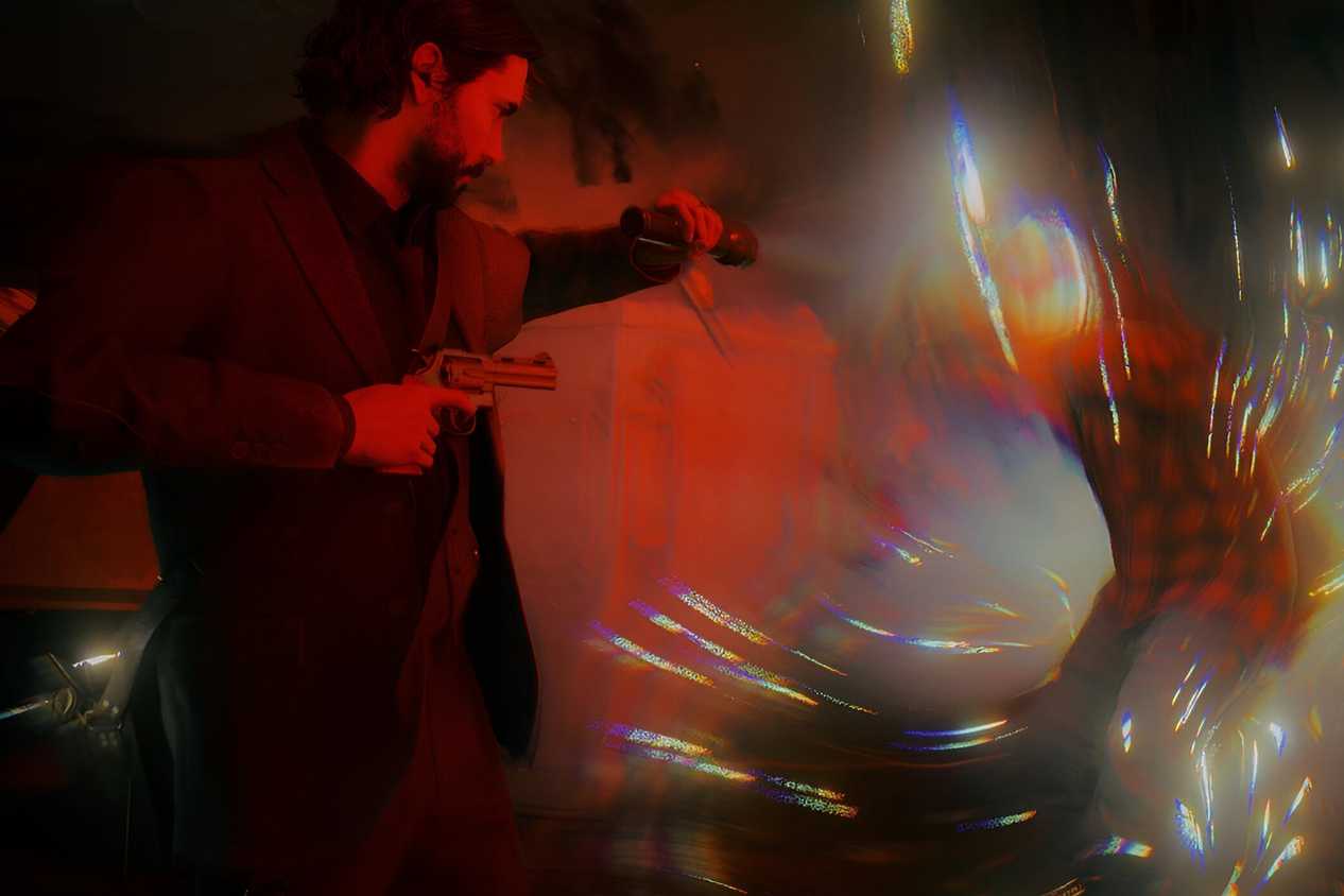 An image from the game "Alan Wake 2", showing a man aiming a flashlight at a disintegrating hostile.