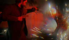 An image from the game "Alan Wake 2", showing a man aiming a flashlight at a disintegrating hostile.