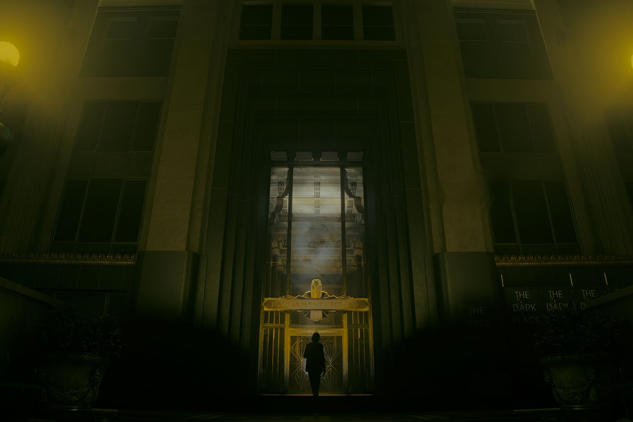 An image from the game "Alan Wake 2", showing a huge building bathed in dim yellow light.