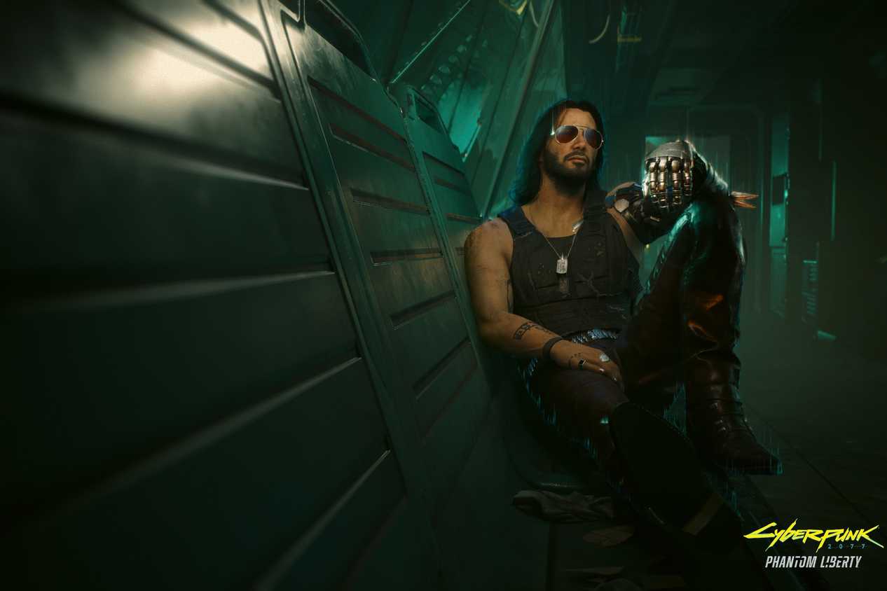 An image from the game "Cyberpunk 2077", showing a man with long hair and sunglasses sitting against a wall in a dimly-lit hallway.
