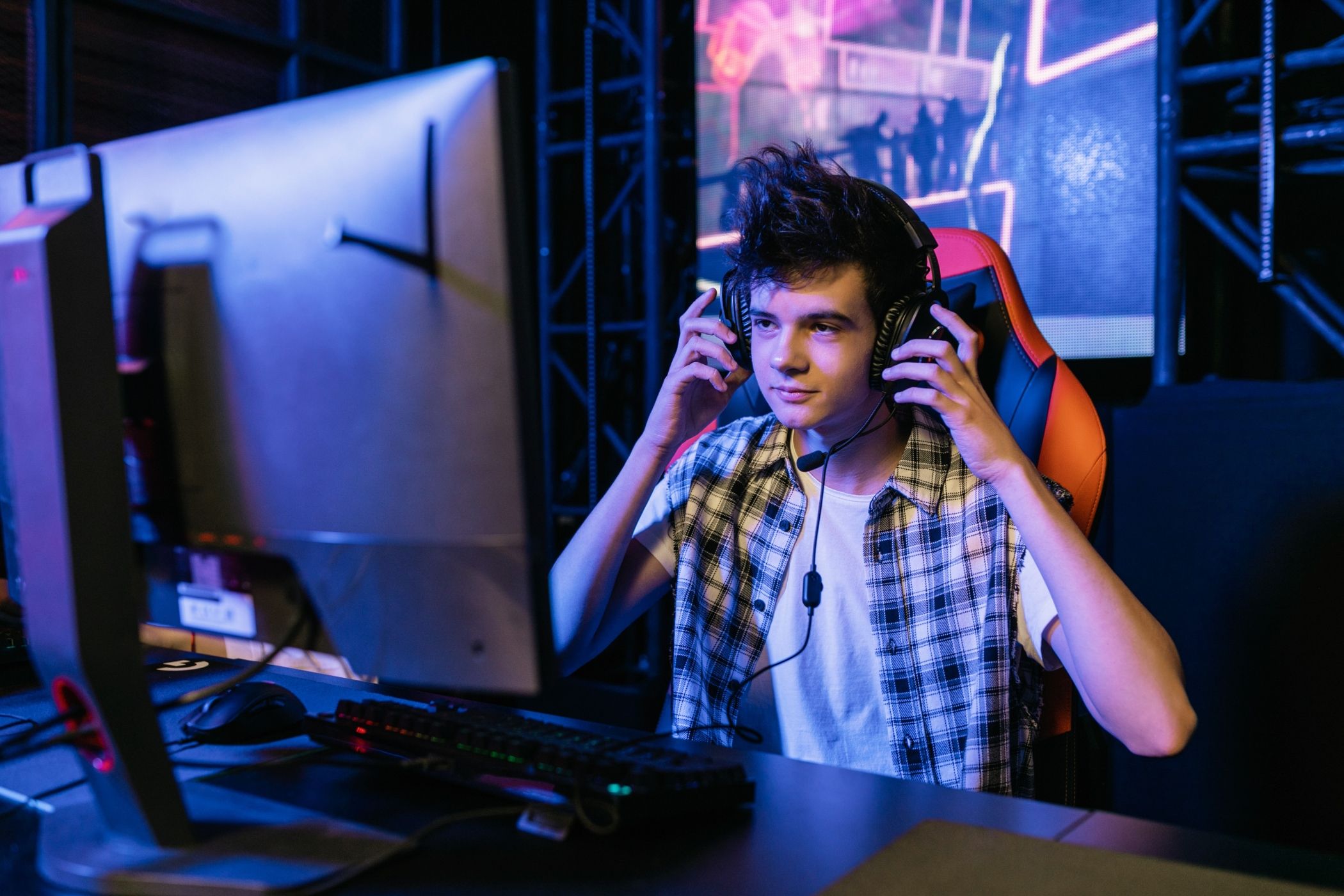 An image of a gamer sitting in front of their PC while touching their over-the-ear headphones
