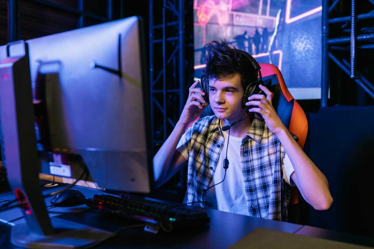 An image of a gamer sitting in front of their PC while touching their over-the-ear headphones