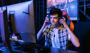 An image of a gamer sitting in front of their PC while touching their over-the-ear headphones