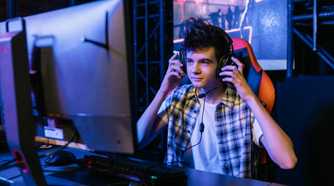 An image of a gamer sitting in front of their PC while touching their over-the-ear headphones