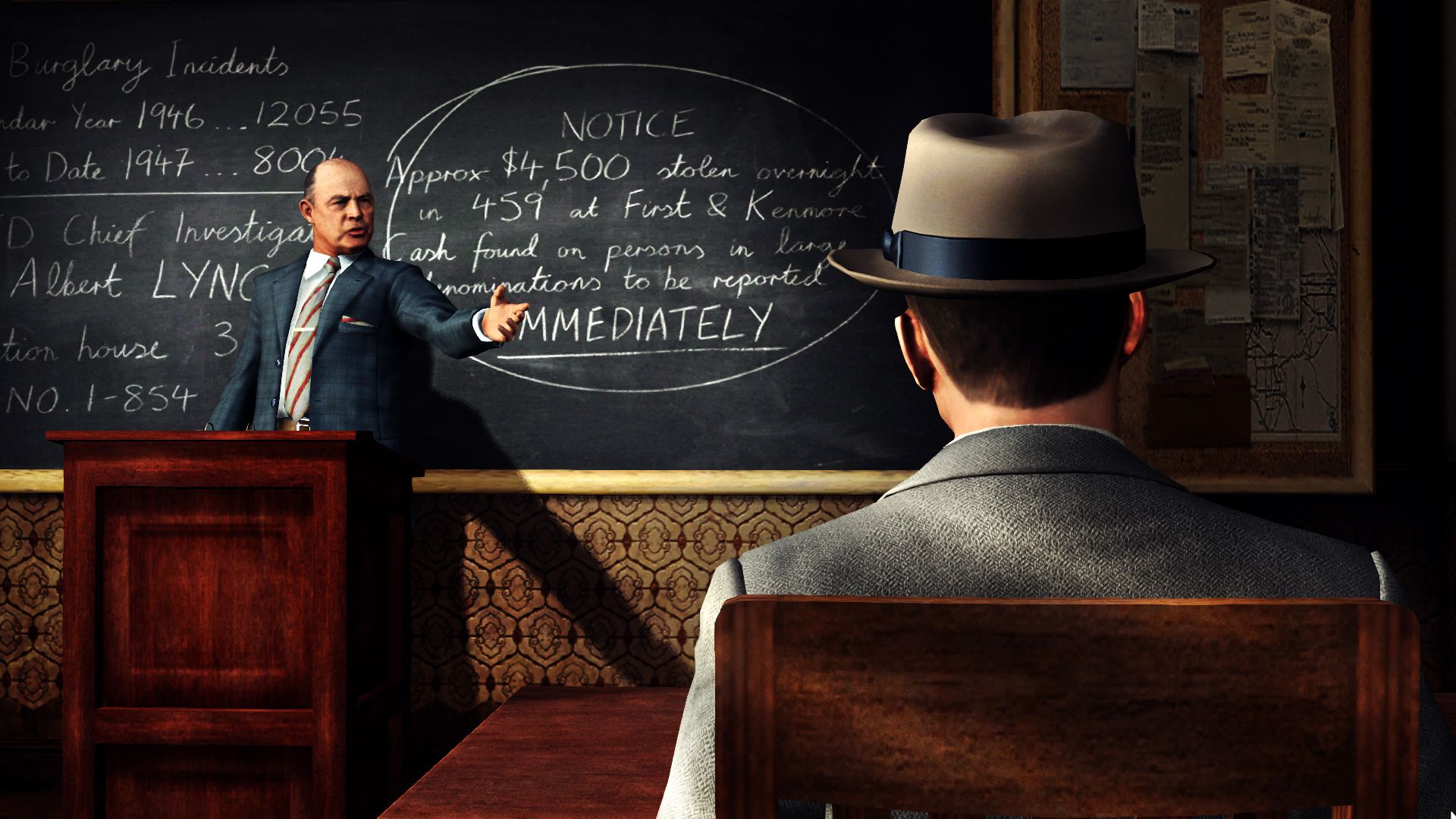 Screenshot from LA Noire video game of two men in 1940's attire talking in boardroom setting with a chalkboard on the wall.