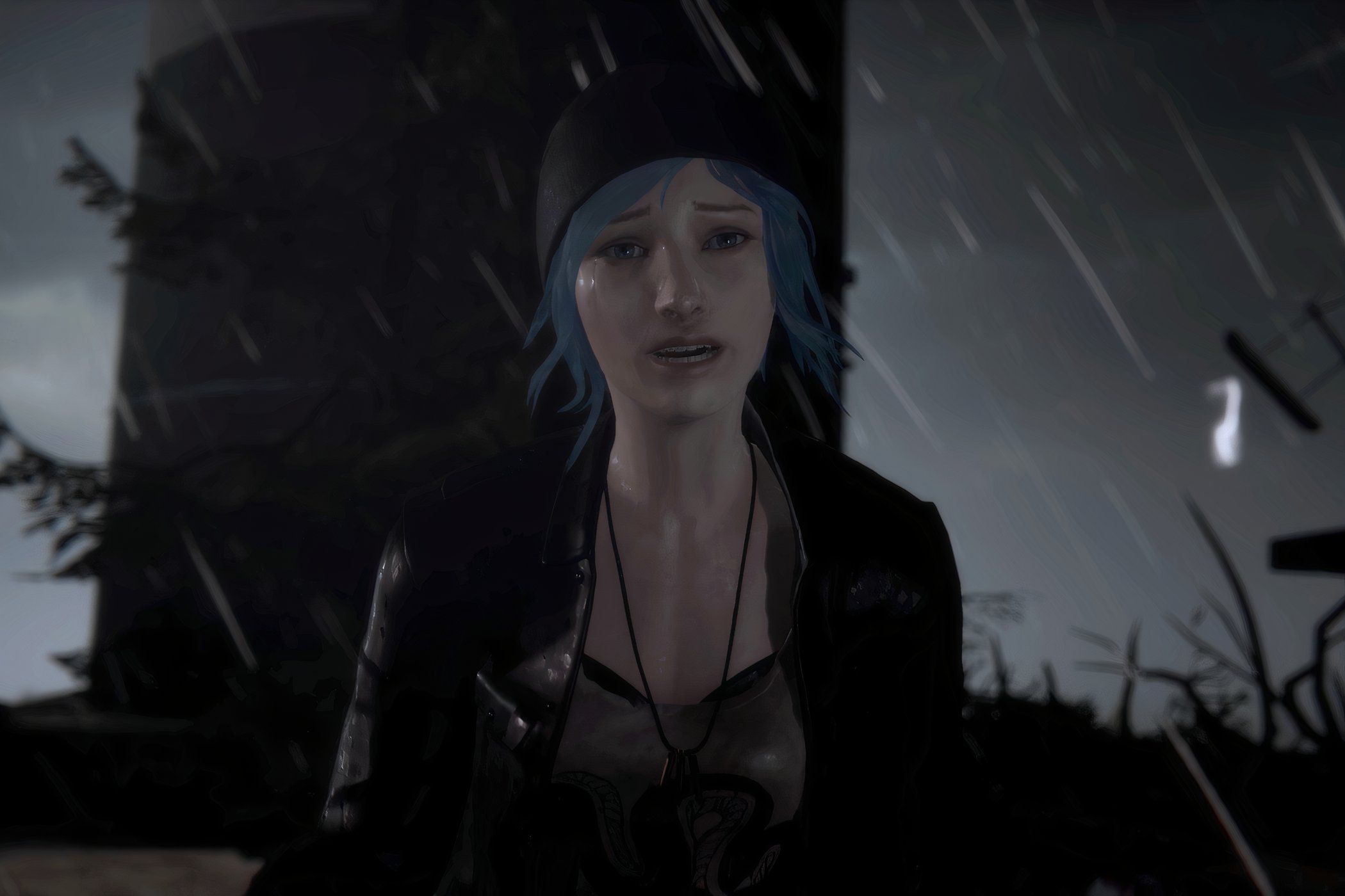 An image from the game Life is Strange, showing a blue-haired girl wearing a beanie and a jacket looking emotional as rain pours down around her.