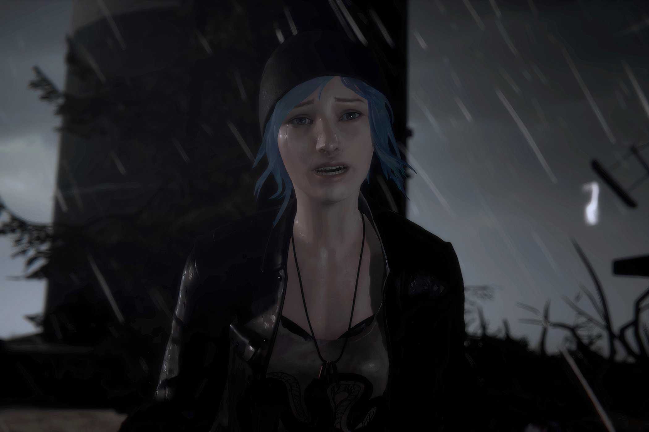 An image from the game Life is Strange, showing a blue-haired girl wearing a beanie and a jacket looking emotional as rain pours down around her.