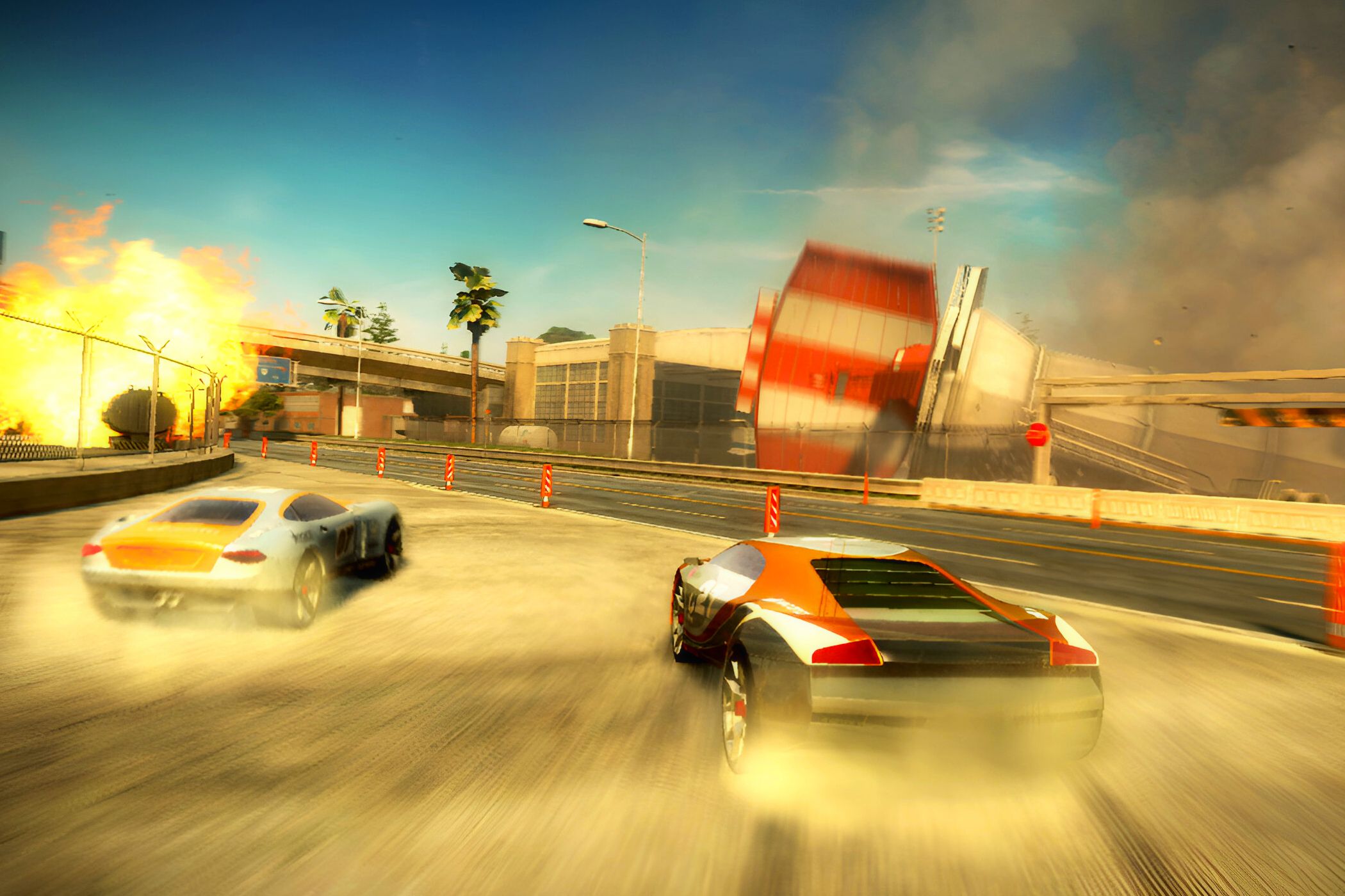 An image from the game "Split Second", showing two cars drift on sand as an airport terminal goes through destruction around them.