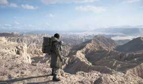 An image from the game Death Stranding 2: On The Beach, showing Sam Porter Bridges looking at a huge arid desert expanding to the horizon.
