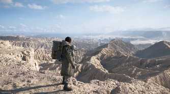 An image from the game Death Stranding 2: On The Beach, showing Sam Porter Bridges looking at a huge arid desert expanding to the horizon.