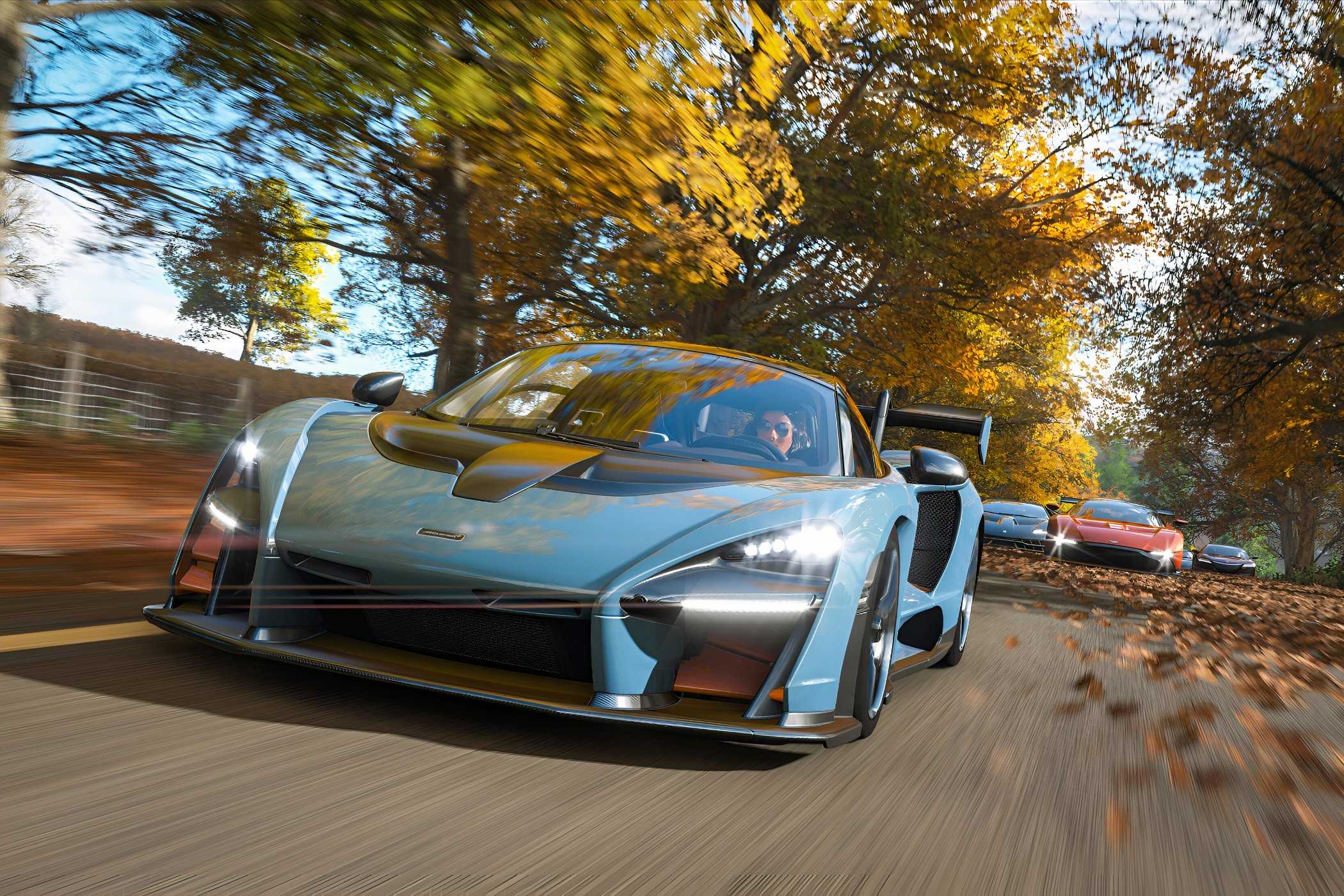 A screenshot from the game "Forza Horizon 4", showing a blue McLaren Senna racing against its competitors during fall season.