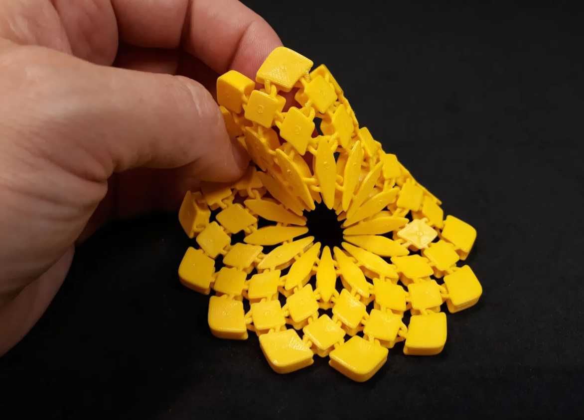 A hand holding a yellow 3D printed sunflower fabric coaster