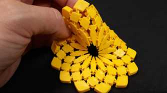 A hand holding a yellow 3D printed sunflower fabric coaster