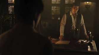 An image from the game Mafia: The Old Country, showing two men talking to each other indoors.