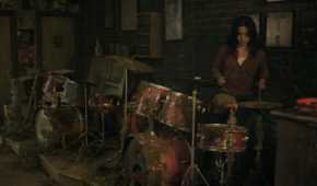 A screengrab from episode 4 of the HBO show The Last of Us Season 2, showing Dina playing the drums inside a music shop.